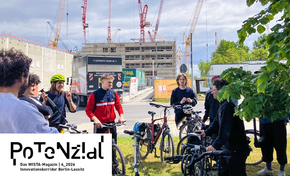 Menschen mit Fahrrädern stehen vor der Baustelle eines Rohbaus