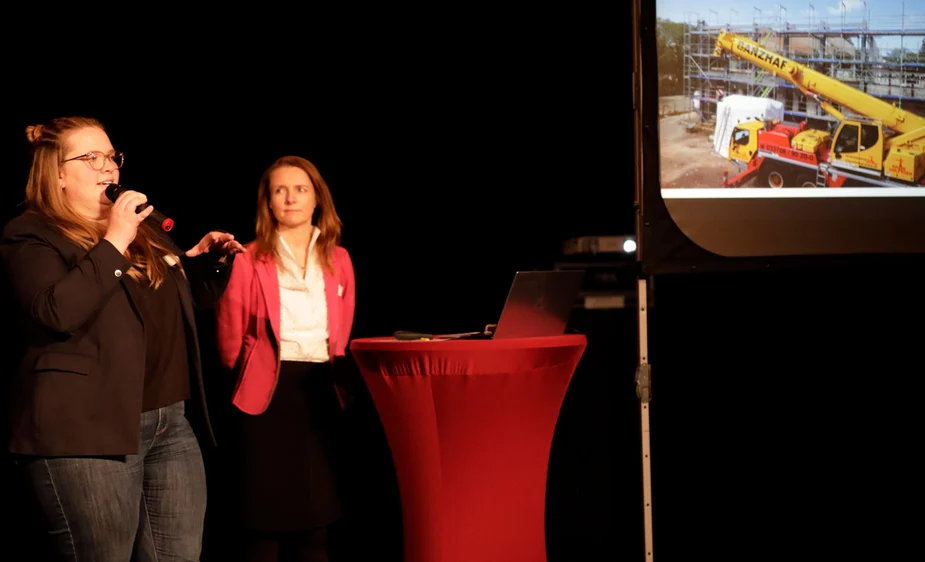 Tina Darley und Stephanie Scheu stehen am Podium und berichten