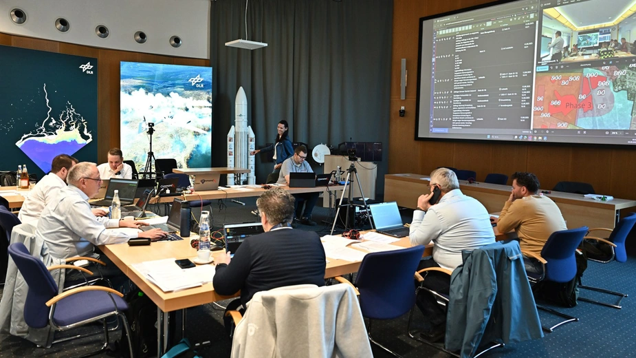 Teilnehmende sitzen in einem Konferenzraum an Laptops, auf dem Monitor ist ein Lageplan sowie der Raum des Stabs zu sehen.