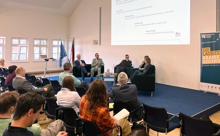 5 Personen diskutieren auf der Bühne vor Publikum