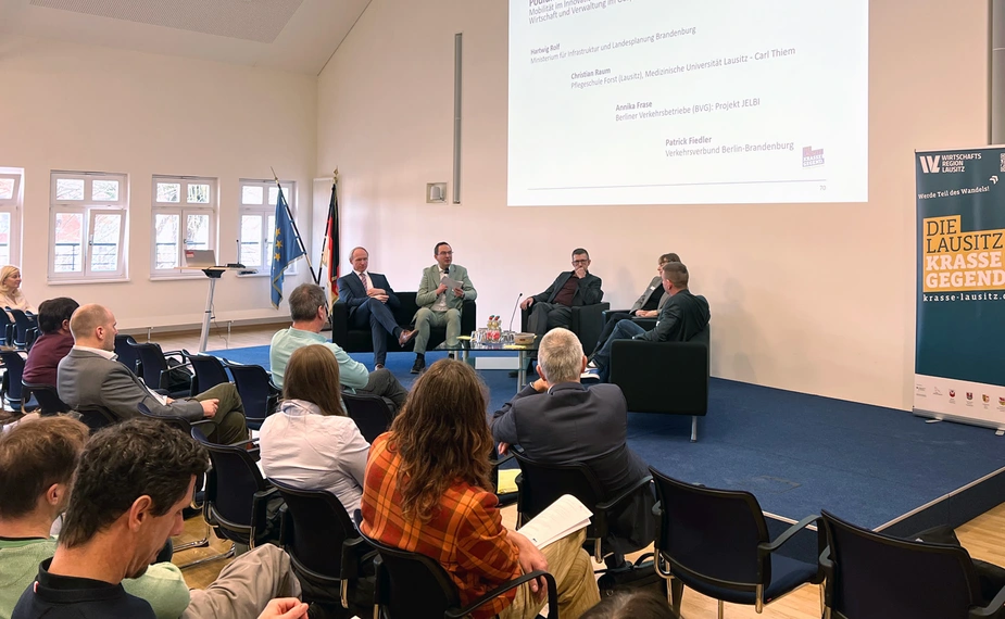 5 Personen diskutieren auf der Bühne vor Publikum