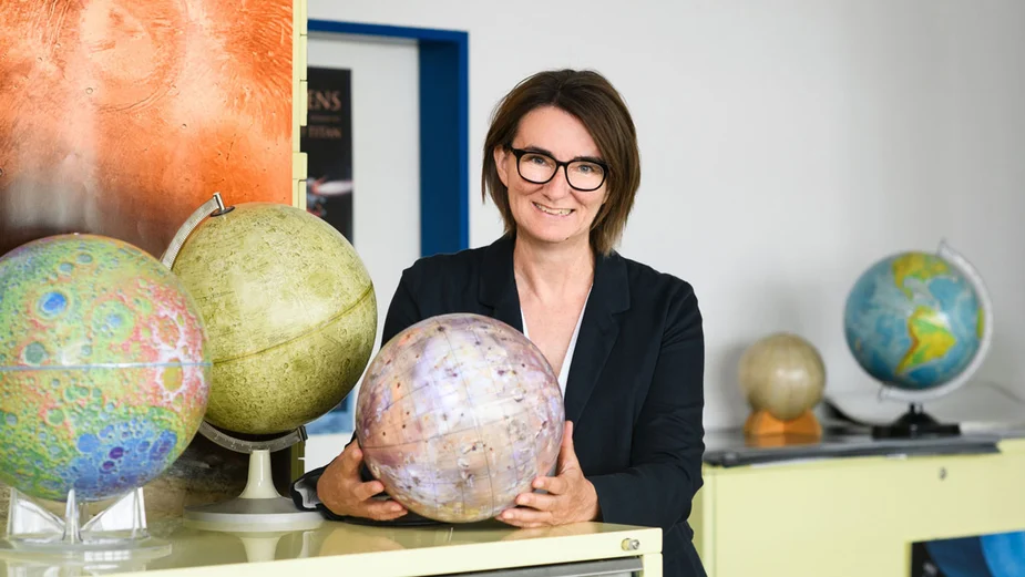Heike Raue mit mehreren Globen verschiedener Planeten