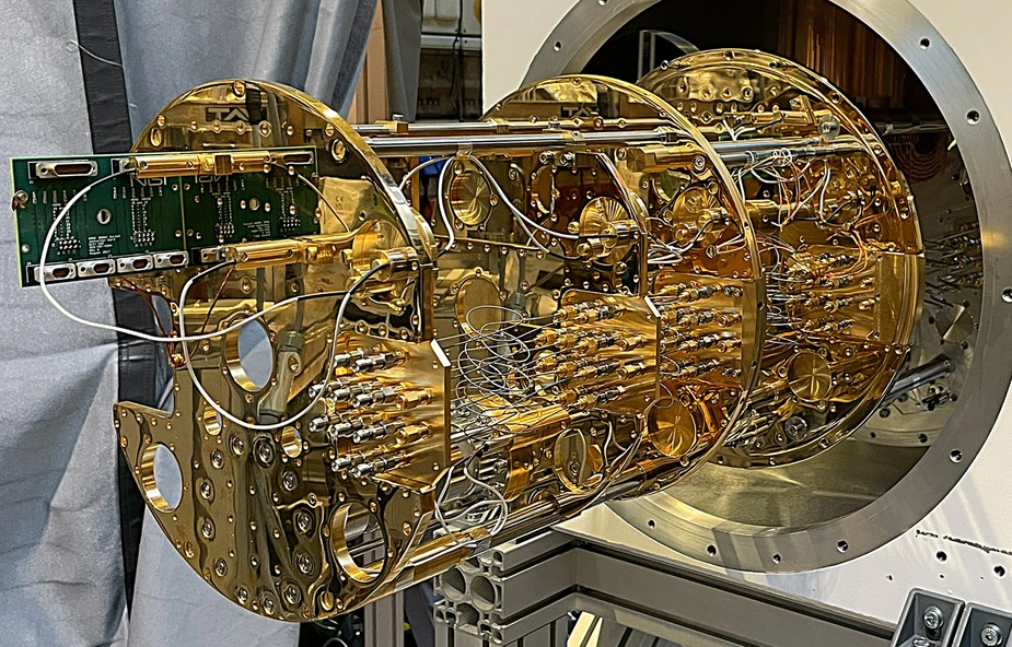 Goldfarbener Kryostat mit zahlreichen Drähten und Kabeln, montiert in einem großen, runden Gehäuse