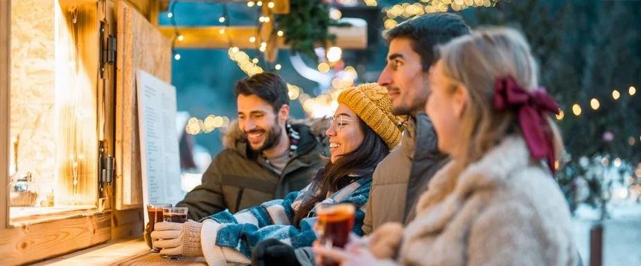 Four people at a festively lit drinks stall in winter