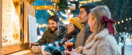 Four people at a festively lit drinks stall in winter