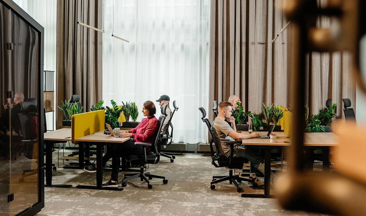 Zwei gegenüberliegende Schreibtische, an denen Personen sitzend arbeiten.