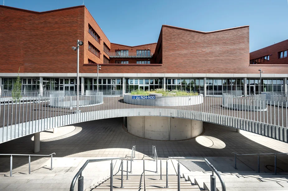 Schulgebäude mit großem, geschwungenem Plateau und einer Freitreppe ins Untergeschoss