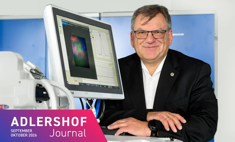 Ein Mann mit Brille steht lächelnd hinter einem Monitor. Im Vordergrund steht ein technisches Gerät.