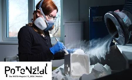 A woman wearing a face mask and blue gloves is working on a white block of stone, whilst dust swirls up