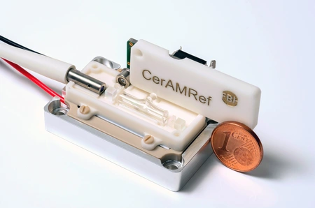 Module, consisting of white plastic parts, a metal cylinder, and connectors. A cent coin is placed next to it for size comparison.