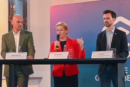 Drei Personen mit Namensschildern am Podium