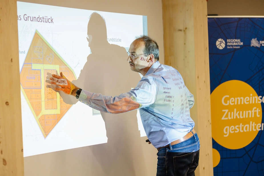 Jörg Israel zeigt auf ein Bild mit dem Grundriss des FUBIC-Campus